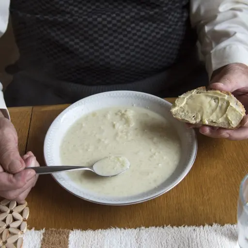 Äldre man äter soppa och smörgås.
