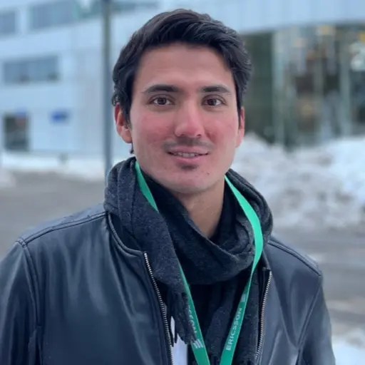 En person står framför en snötäckt gata med moderna byggnader i bakgrunden. Till höger syns en skylt med texten 'Ericsson Group Headquarters' och företagets logotyp, upplyst i mörker.