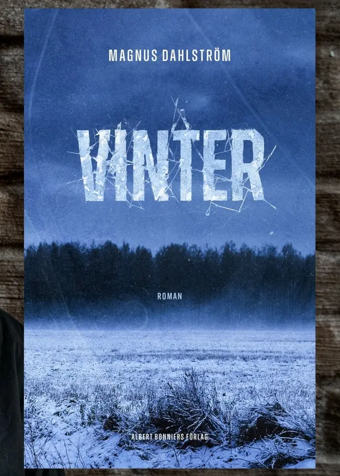Magnus Dahlström står framför en mörk bakgrund med en boktitel, ”Vinter” av Magnus Dahlström, synlig bredvid. Bokens omslag visar ett snötäckt landskap med träd i fjärran.