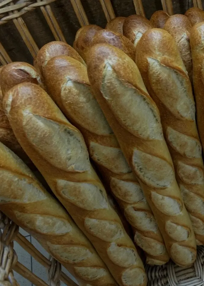 Ett franskt militärfartyg, Charles de Gaulle, ligger vid kaj med stridsflygplan på däck. Bredvid syns en korg med nybakade baguetter. Bilden kombinerar maritim och fransk kultur.