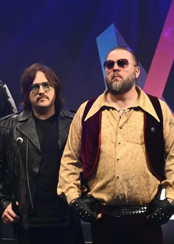 Fem medlemmar i bandet Korslagda står på en scen under en pressträff för Melodifestivalen 2026. De är klädda i rockinspirerade kläder och en glittrande discokula hänger ovanför dem.