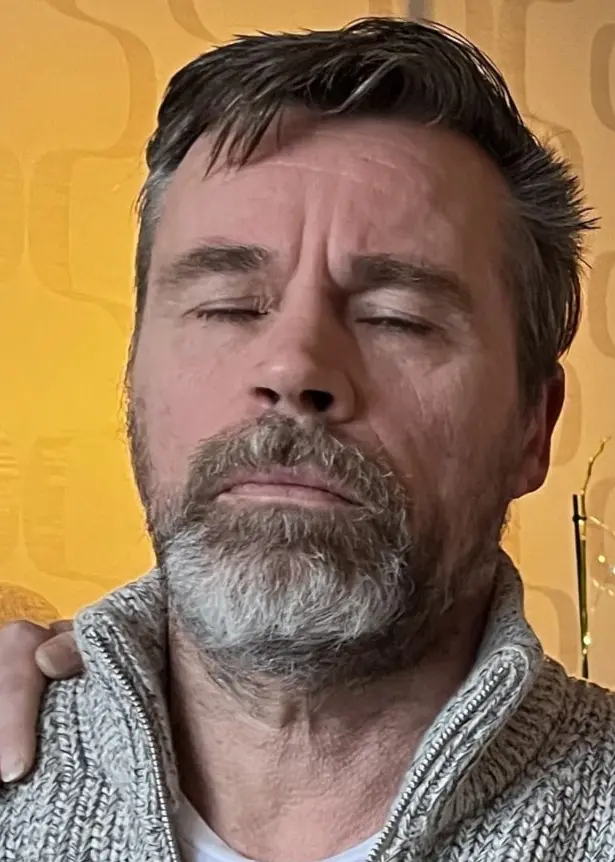 En man och en kvinna sitter tillsammans i ett vardagsrum. Mannen blundar och kvinnan tittar bort mot ljuset från ett fönster. Hon håller sin ena arm kring mannen. Han har kort hår och ett silvrigt, ganska kort skägg. Hon har blont uppsatt hår. Dom har ljusa kläder.