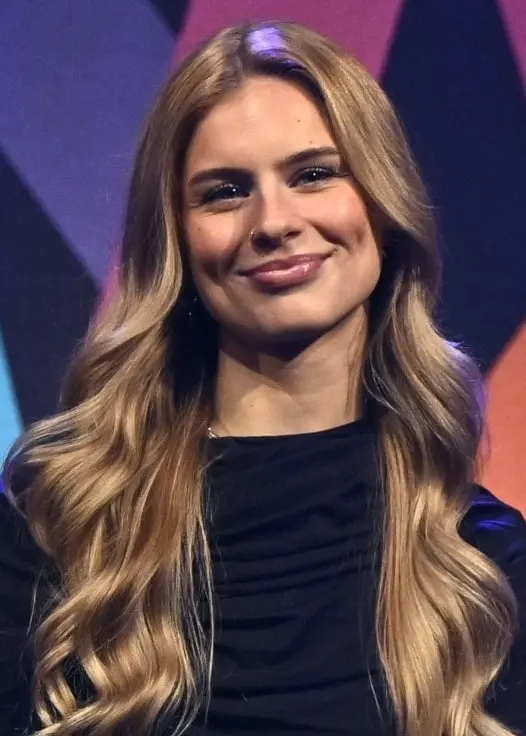 Kvinna med långt, mörkblont hår framför Melodifestivalloggan.