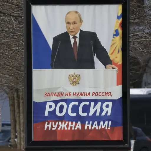 Två personer promenerar förbi en reklamskylt med en bild av Rysslands president Vladimir Putin och en text som uppmanar till stöd för Ryssland. Skylten står på en gata i Sevastopol, Krim.