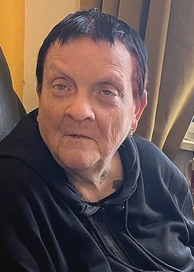 Ann Kurki sitter på en svart läderfåtölj i ett rum med gula väggar. Ett fönster med persienner och flera pennor och kontorsmaterial syns på en hylla vid fönstret.