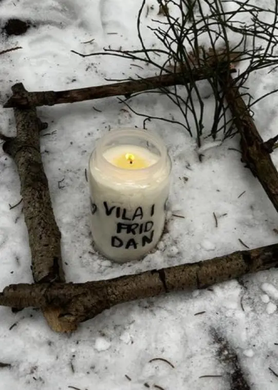 Ett ljus omgivet av pinnar i snön, med texten ”Vila i frid” skriven på ljuset.