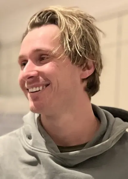 Två personer skakar hand i en ljus inomhusmiljö med bord och stolar i bakgrunden. Den ena personen bär en mörk jacka, och den andra har en grå hoodie.