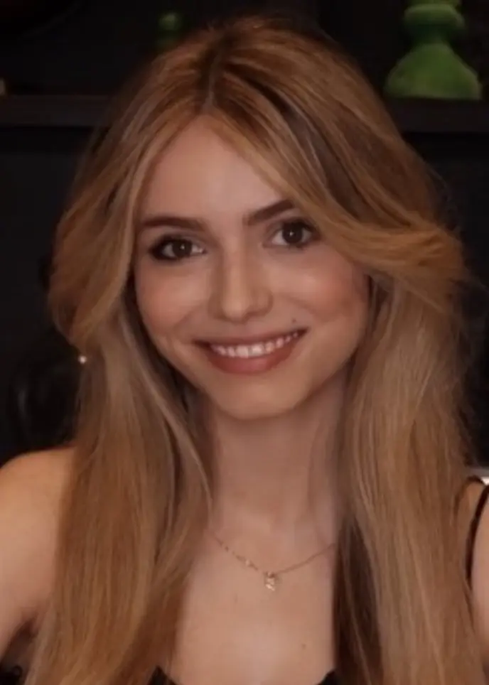 En schackbräda med vit schackpjäser uppställda för spel, fotograferad i närbild. Till höger syns en person med långt blont hår, klädd i en svart klänning.