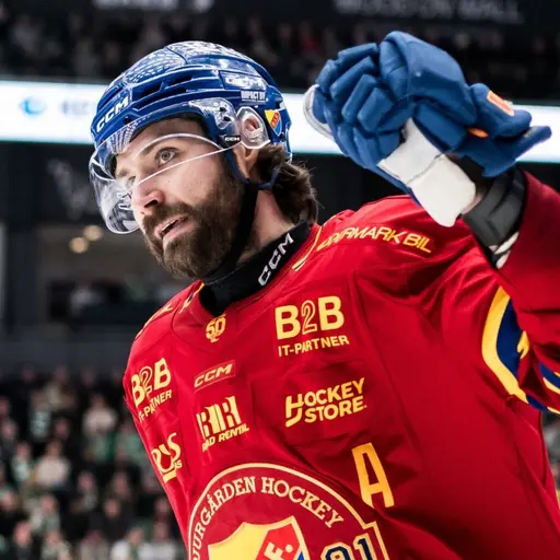 En ishockeyspelare i röd matchtröja med nummer 91 och ett A på bröstet höjer sin arm i en segergest på isen. Bakgrunden visar en arena med publik och reklamskyltar.