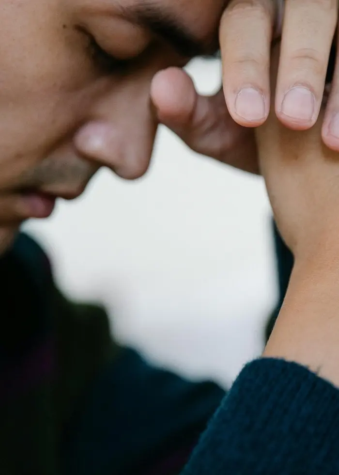 En person håller händerna ihop över ett svart mikrofonstativ. Bakgrunden är suddig och neutral.