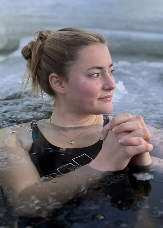 Marlene Claussen i baddräkt badar i iskallt vatten omgivet av isflak. Händerna är sammanlagda framför kroppen, och miljön är en kall vinterdag vid en isvak.