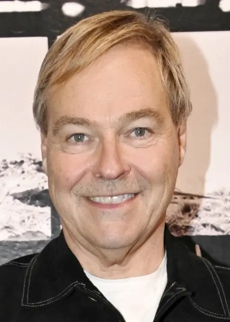 En person står framför en vägg med svartvita fotografier som föreställer historiska scener, inklusive militärfordon och människor i olika miljöer. Personen bär en mörk jacka.