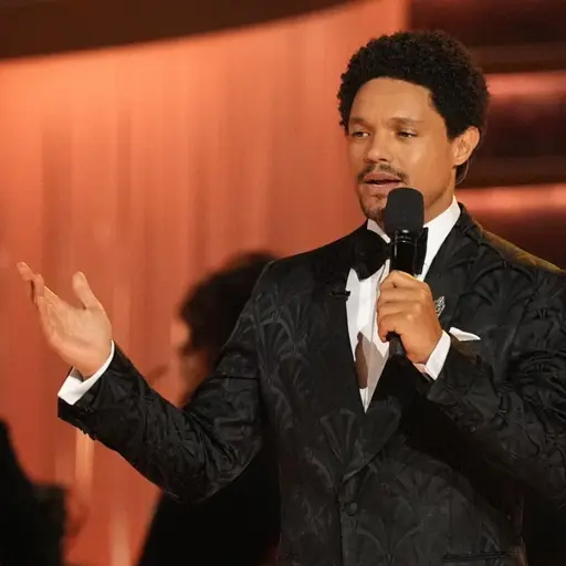 En person i elegant kostym håller ett tal på en scen under Grammy Awards. Bakgrunden är upplyst i varma toner med sittande publik i mörka kläder.