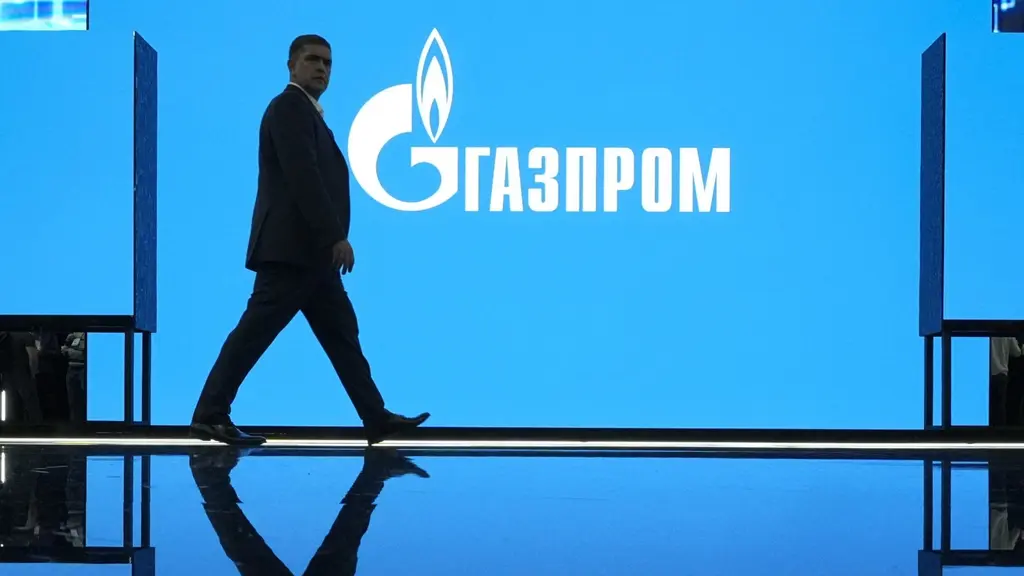 En man promenerar framför en stor blå skärm med Gazproms logotyp under en utställning på internationella gasforumet i Sankt Petersburg, Ryssland. Reflektioner syns på en blank yta nedanför.