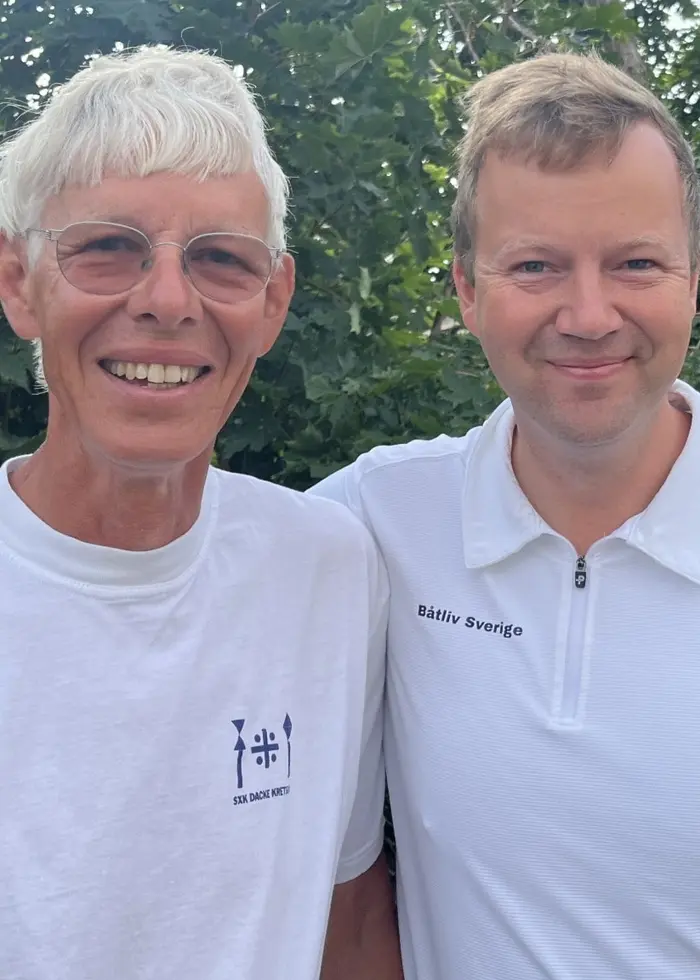Pär Svensson och Fredrik Norén står sida vid sida utomhus i vita tröjor, framför grönska och trädgårdsmiljö.