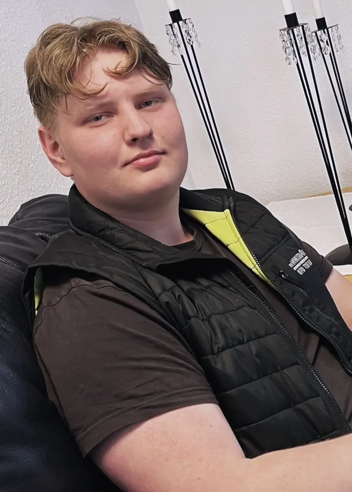 Hugo Johansson sitter i en svart skinnfåtölj i ett vardagsrum, klädd i svart väst och jeans.