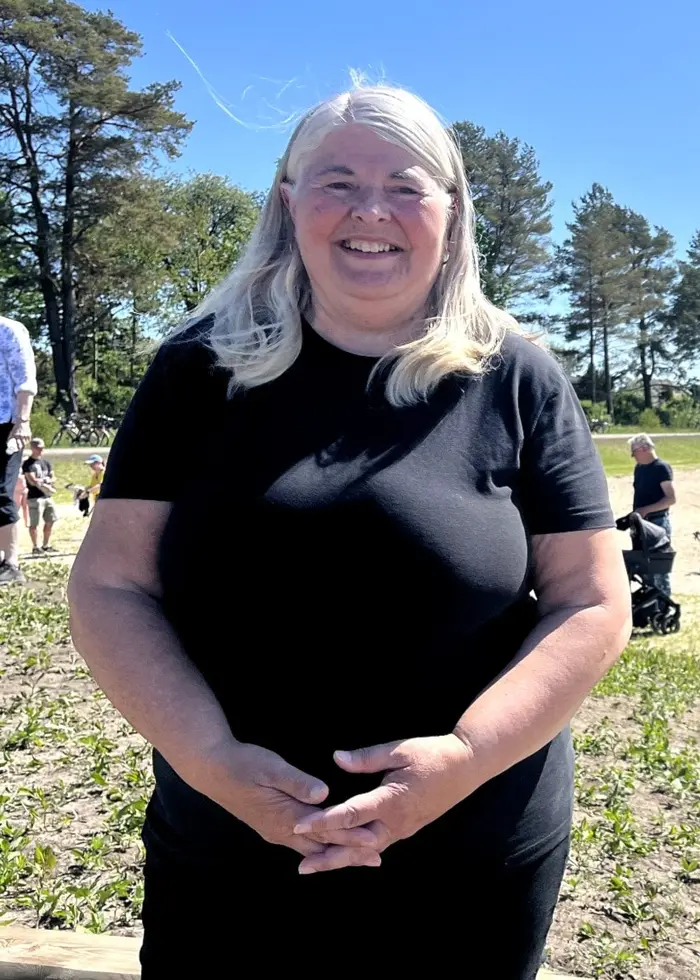 En kvinna i svarta kläder på en sandstrand till en badsjö.