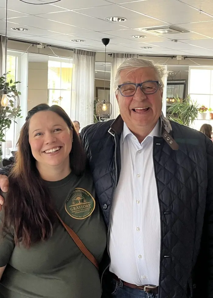 Sara Bäcklin och Per Hansson står tätt tillsammans i Fram för kommunens partilokal, ett ljust fik med bord, växter och gäster i bakgrunden.
