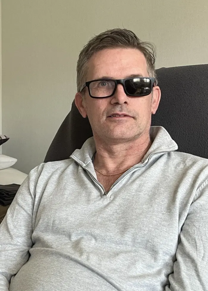 Kvinna med långt, blont hår och vit tröja sitter bredvid man med ljusgrå tröja och glasögon där ena glaset är svart.